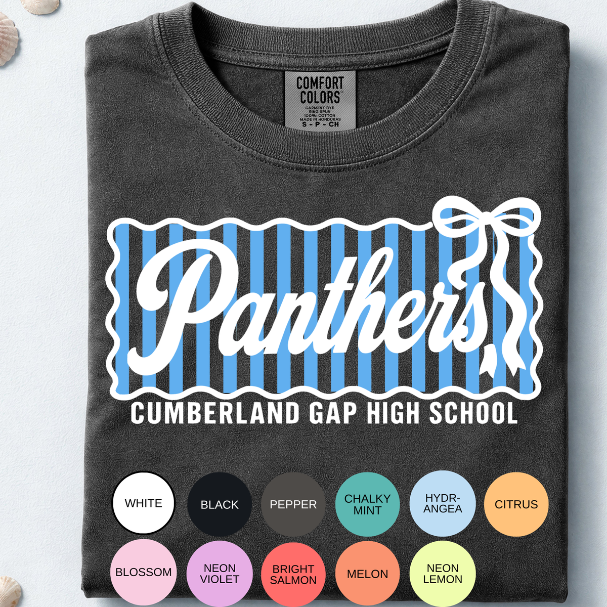A folded white Comfort Colors t-shirt with a light blue and gray 'Panthers Cheer Cumberland Gap High School' graphic, styled on a light blue background with seashells.