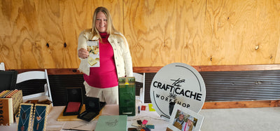 Cheryl holding a product in front of a 'The Craft Cache Workshop' sign. Taken at WEdding open house at New Haven Farm in Jacksboro, TN.