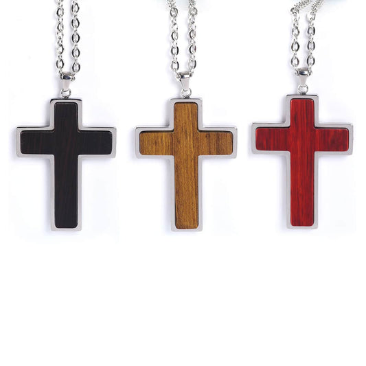 Three cross-shaped pendants in black, wood, and red on silver chains against a white background.